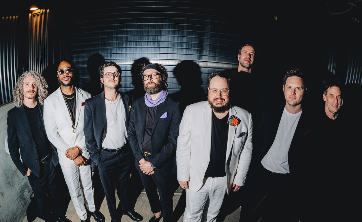 Soul band St. Paul & The Broken Bones members lining up together in black and white suits in front of a shutter door.